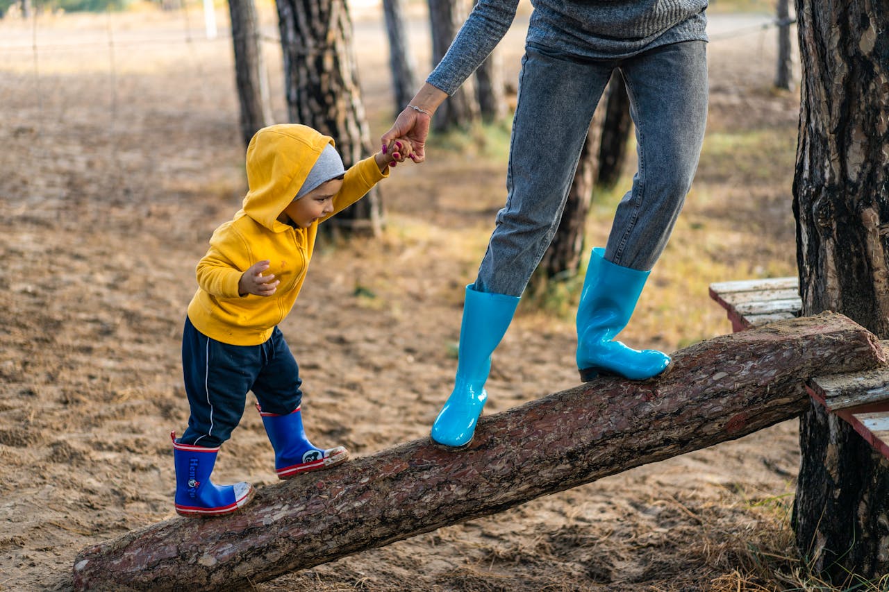 our-services-3 A woman helps her toddler walk on a log in a park, showcasing child support and family bonding.