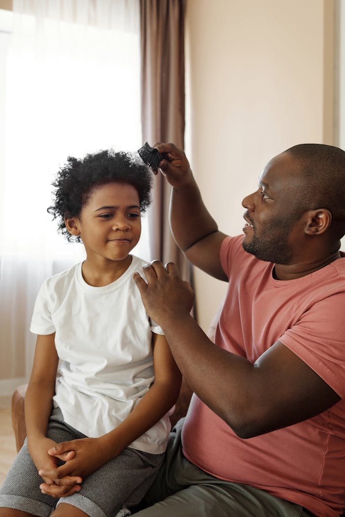 A father brushes his son's curly hair, showcasing love and parenthood indoors.
